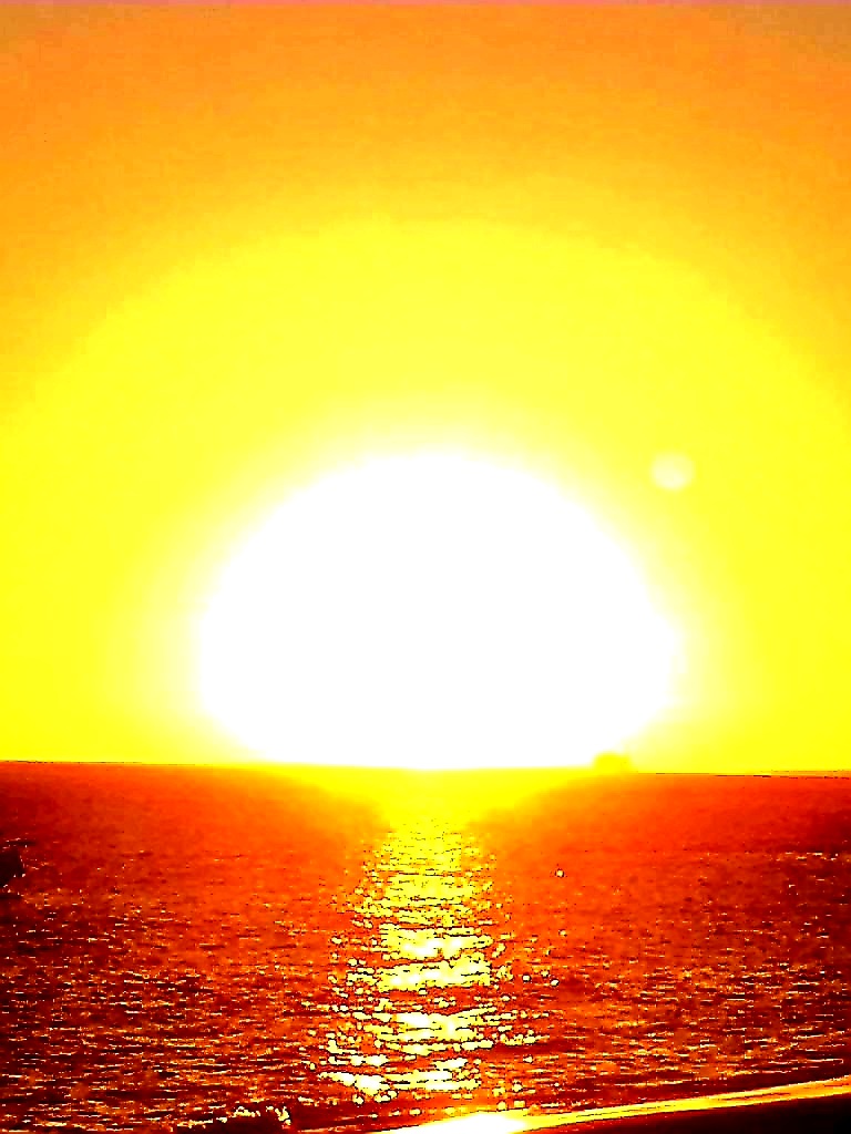 Zurück ins Licht: Dieses Foto von einem Sonnenuntergang am Meer  mit einer riesigen, hellen Sonne in der Bildmitte und in strahlenden Gelb- und Orangetönen ist die perfekte Illustration.