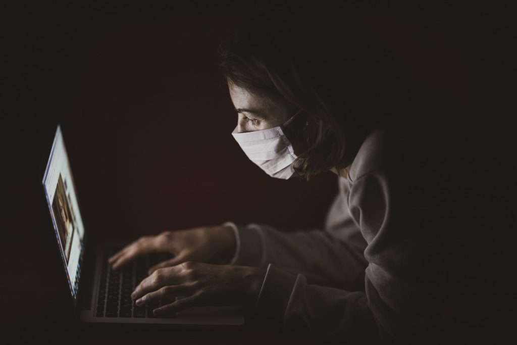 Zuhausebleiben: Eine Frau mit Maske vor dem Laptop.