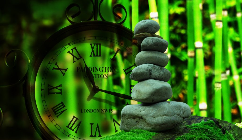 Die Lebenszeit am Beispiel einer Uhr und aufeinandergeschichteter Steine vor dem Hintergrund eines Bambus.
