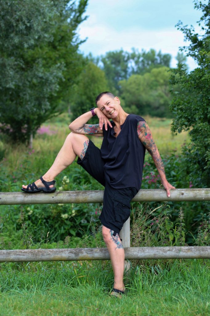 Sabine Scholze, 60plus, sitzt auf enem Geländer im Grünen und lächelt.
